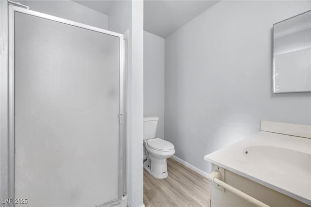 bathroom with toilet, a stall shower, wood finished floors, baseboards, and vanity