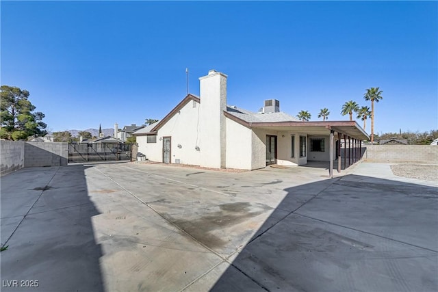 back of house featuring a patio, a gate, fence, a chimney, and stucco siding