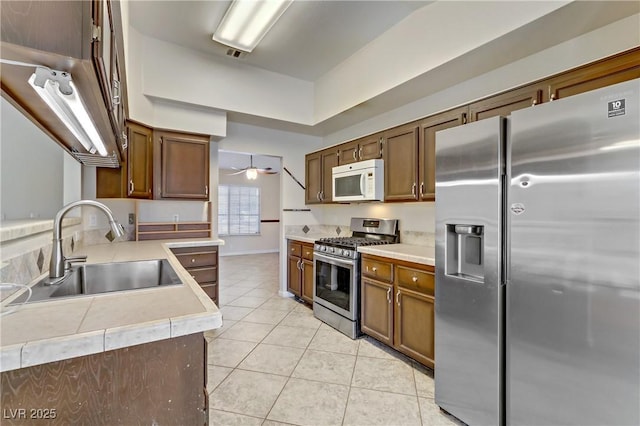 kitchen with a sink, appliances with stainless steel finishes, light countertops, light tile patterned floors, and ceiling fan