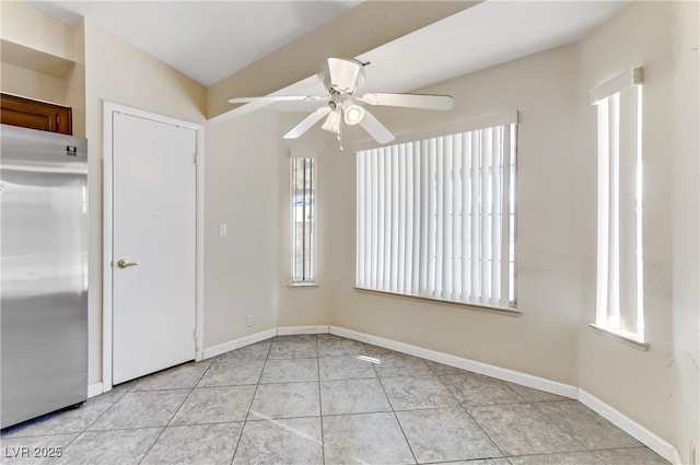 empty room with a ceiling fan, plenty of natural light, light tile patterned flooring, and baseboards