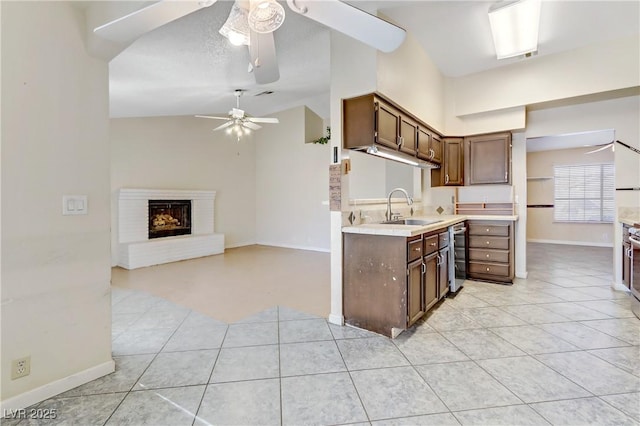 kitchen featuring a brick fireplace, ceiling fan, light countertops, vaulted ceiling, and a sink