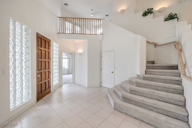 entryway featuring stairway, light tile patterned floors, a ceiling fan, visible vents, and a high ceiling