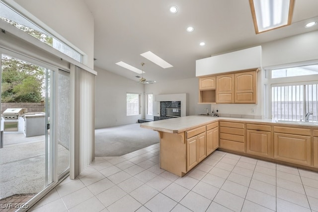 kitchen featuring light brown cabinetry, open floor plan, light countertops, a glass covered fireplace, and a sink