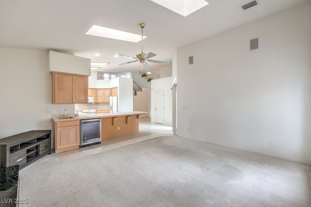 kitchen with white appliances, beverage cooler, visible vents, light brown cabinets, and light colored carpet