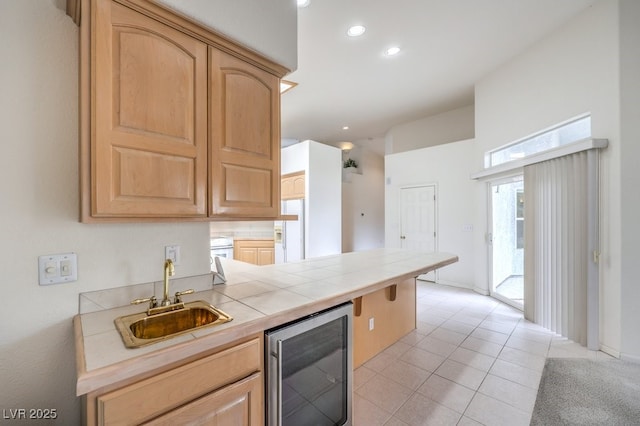 kitchen with light tile patterned floors, beverage cooler, light brown cabinets, a sink, and tile counters