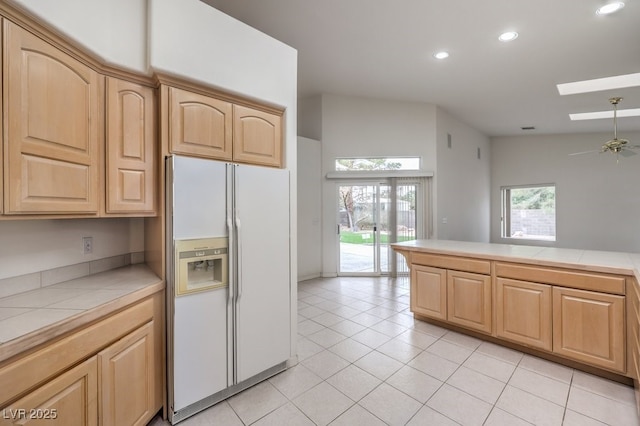 kitchen featuring tile counters, light brown cabinetry, lofted ceiling with skylight, light tile patterned floors, and white refrigerator with ice dispenser