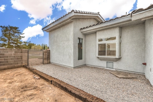 view of side of property featuring a gate, stucco siding, a tiled roof, and fence