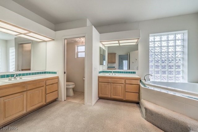 bathroom with two vanities, toilet, tiled bath, and a sink