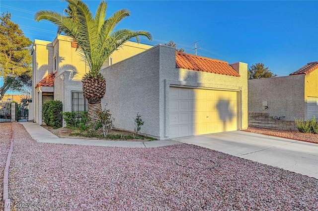 view of side of home with a tiled roof, stucco siding, a garage, driveway, and a gate