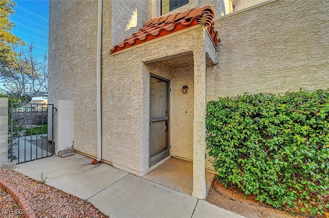 view of exterior entry with a gate, stucco siding, and a tiled roof