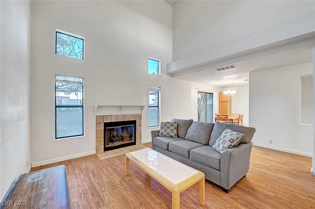 living area with visible vents, a notable chandelier, light wood-style flooring, baseboards, and a tile fireplace