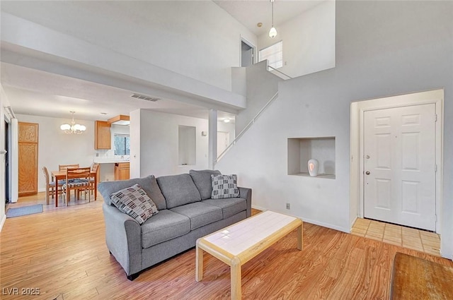 living area featuring visible vents, light wood-style flooring, a towering ceiling, and a chandelier