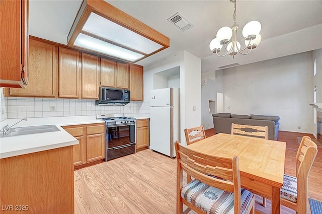 kitchen with visible vents, backsplash, light wood-style flooring, black appliances, and a sink