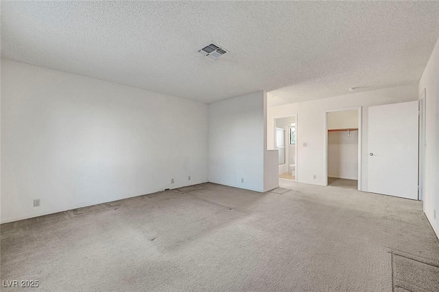 empty room featuring visible vents, light colored carpet, and a textured ceiling