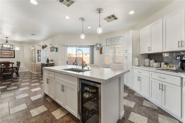 kitchen featuring a sink, visible vents, backsplash, and beverage cooler