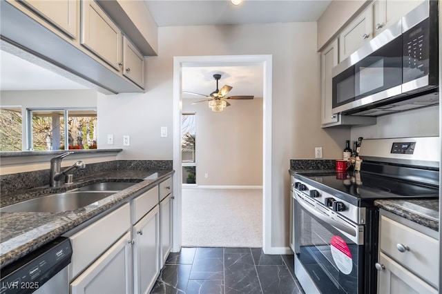 kitchen with dark stone countertops, baseboards, ceiling fan, a sink, and appliances with stainless steel finishes