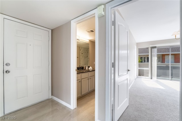 corridor featuring a sink, visible vents, baseboards, and light carpet