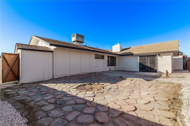 rear view of house featuring a gate, fence, cooling unit, board and batten siding, and a patio area