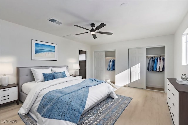 bedroom featuring light wood-type flooring, visible vents, two closets, and a ceiling fan