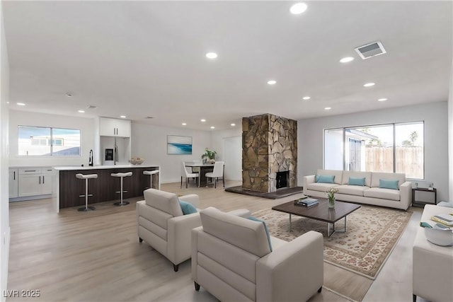 living area featuring light wood finished floors, visible vents, recessed lighting, and a fireplace