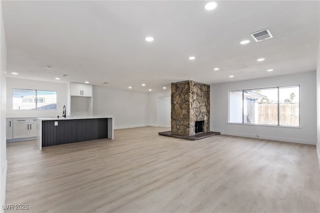 unfurnished living room featuring recessed lighting, visible vents, a stone fireplace, and light wood-style flooring