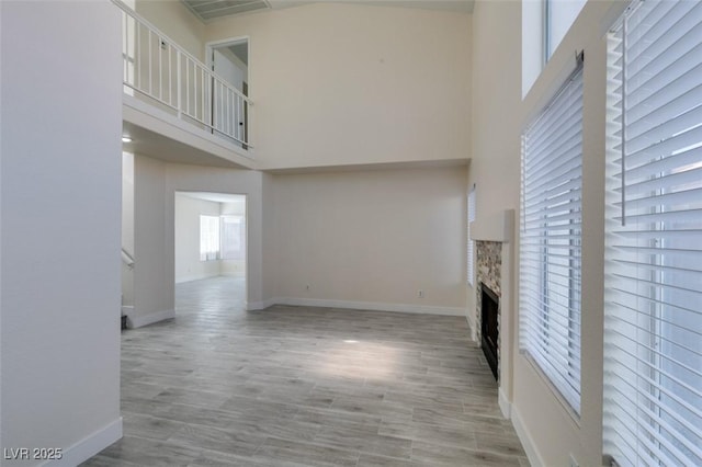 unfurnished living room with wood finished floors, baseboards, visible vents, a high ceiling, and a fireplace