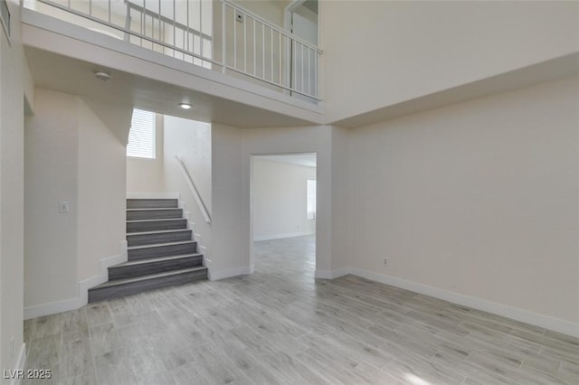 interior space with stairs, a high ceiling, baseboards, and wood finished floors