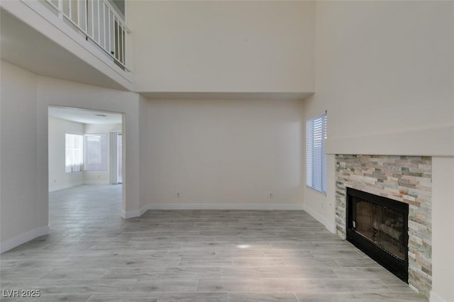 unfurnished living room featuring baseboards, a high ceiling, a stone fireplace, and light wood-style flooring