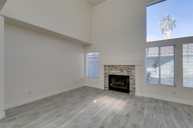 unfurnished living room featuring light wood-type flooring, baseboards, and a stone fireplace