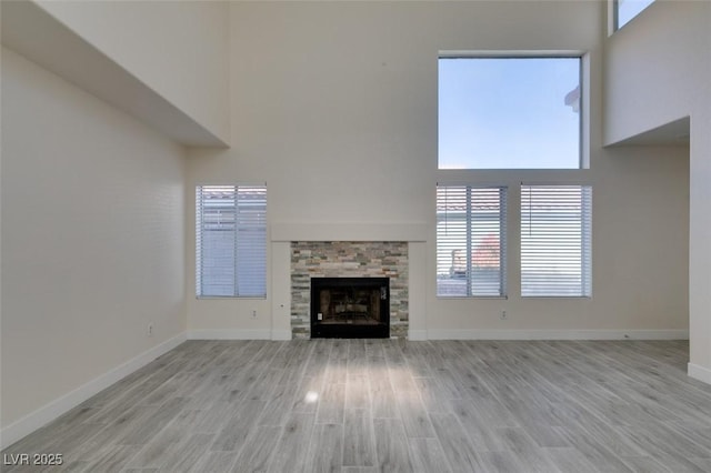 unfurnished living room featuring baseboards, light wood-style floors, a towering ceiling, and a fireplace