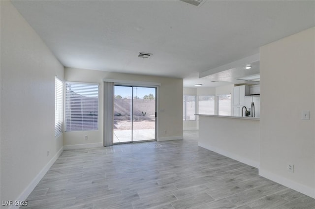 unfurnished living room featuring light wood-style floors, visible vents, and baseboards