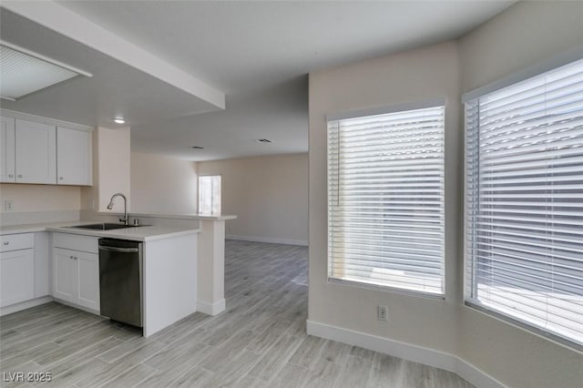 kitchen featuring light wood finished floors, a sink, light countertops, a peninsula, and stainless steel dishwasher