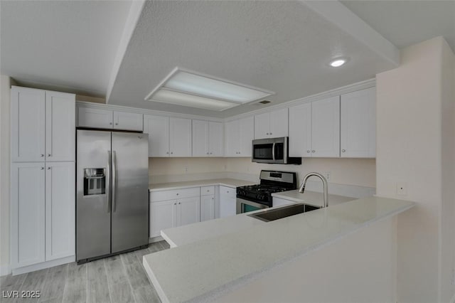 kitchen with light wood finished floors, a sink, stainless steel appliances, light countertops, and white cabinetry