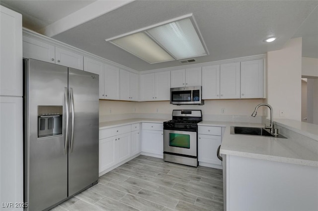 kitchen with a peninsula, a sink, white cabinets, light wood-style floors, and appliances with stainless steel finishes