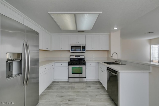 kitchen featuring visible vents, a sink, stainless steel appliances, a peninsula, and light countertops