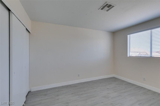 unfurnished bedroom featuring light wood finished floors, visible vents, a closet, and baseboards