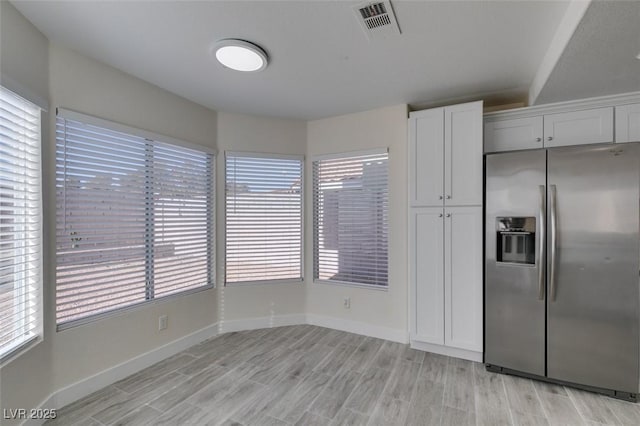 kitchen featuring visible vents, a wealth of natural light, light wood-style flooring, stainless steel refrigerator with ice dispenser, and white cabinets