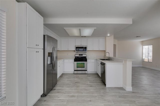 kitchen with open floor plan, light countertops, appliances with stainless steel finishes, a peninsula, and a sink