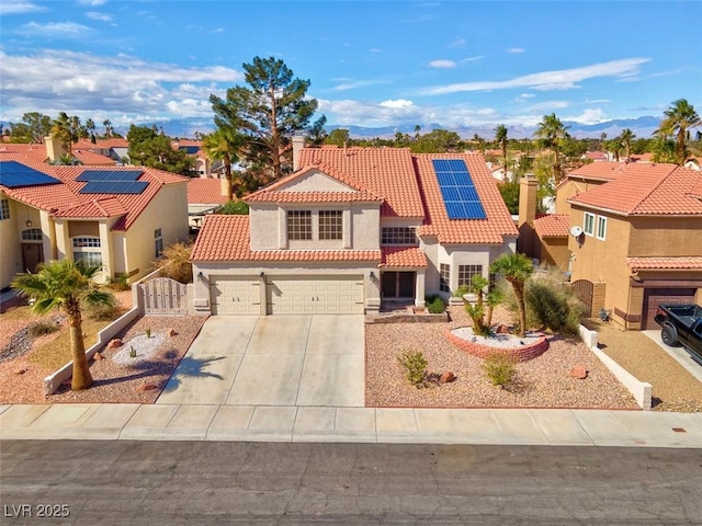 mediterranean / spanish-style home with roof mounted solar panels, a residential view, concrete driveway, stucco siding, and a tile roof