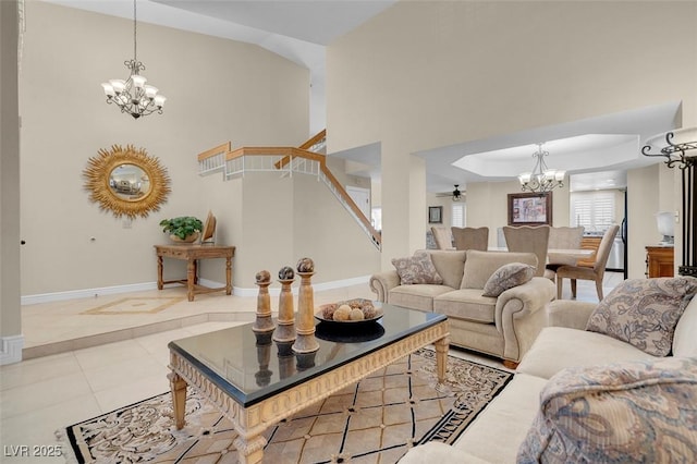 tiled living room with stairs, ceiling fan with notable chandelier, a high ceiling, a raised ceiling, and baseboards