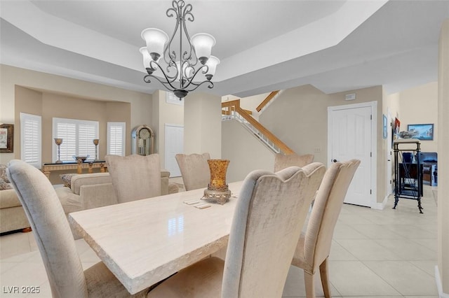 dining area featuring a raised ceiling, a notable chandelier, light tile patterned floors, baseboards, and stairs