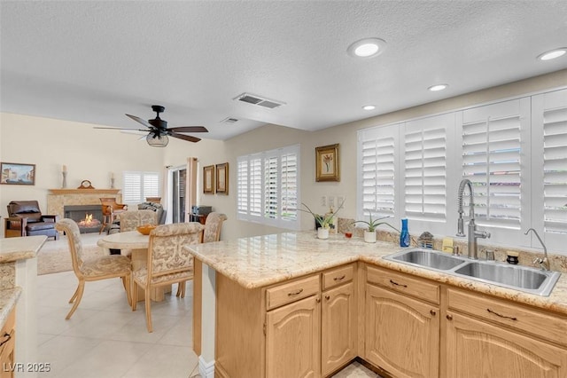 kitchen with a sink, a textured ceiling, ceiling fan, a lit fireplace, and visible vents