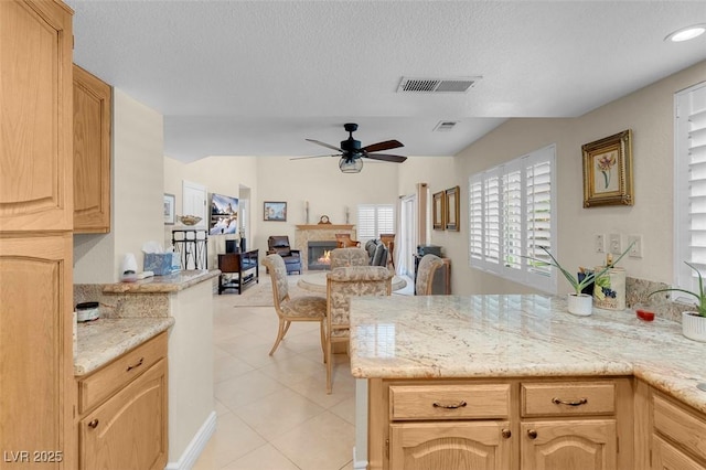 kitchen with visible vents, a ceiling fan, light brown cabinets, open floor plan, and a glass covered fireplace