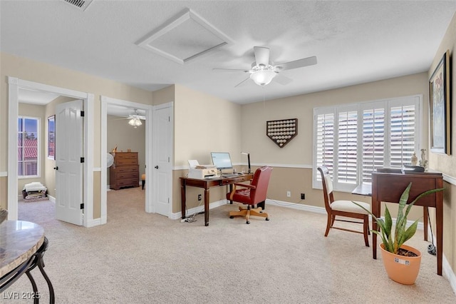 carpeted office space with a textured ceiling, attic access, baseboards, and a ceiling fan