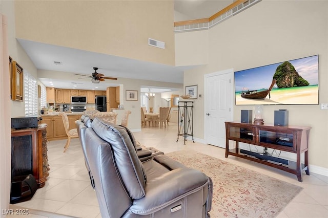 living area featuring visible vents, ceiling fan with notable chandelier, a high ceiling, light tile patterned floors, and baseboards