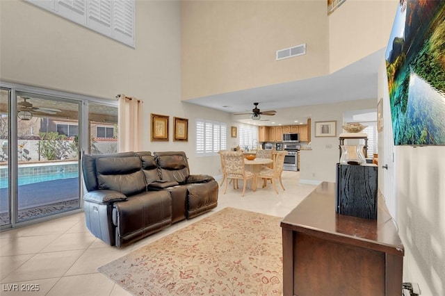 living room with a ceiling fan, visible vents, a high ceiling, and light tile patterned flooring