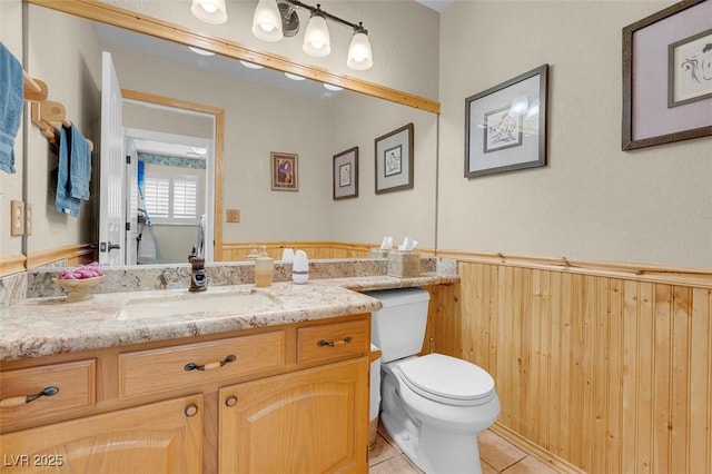 bathroom with toilet, wainscoting, vanity, and tile patterned flooring