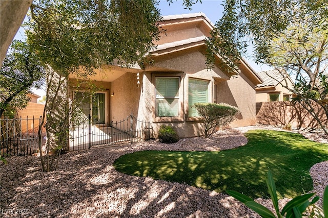 view of front of home with a front yard, a tiled roof, fence private yard, and stucco siding