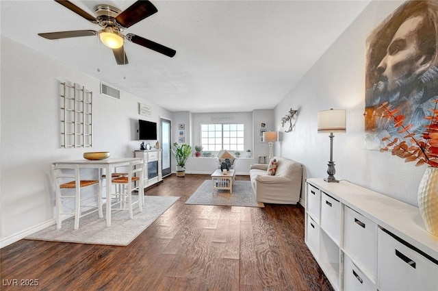 living area with visible vents, baseboards, dark wood-type flooring, and a ceiling fan