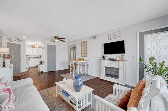 living room with baseboards, visible vents, dark wood-style flooring, ceiling fan, and a glass covered fireplace